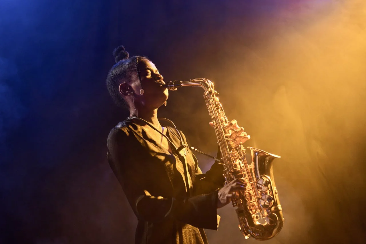 A woman playing saxophone on stage with colorful lighting.