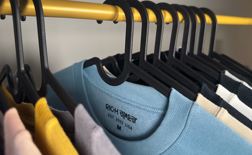 Close-up of a clothing rack with black hangers holding T-shirts in different colors, including blue, beige, and striped black and white.