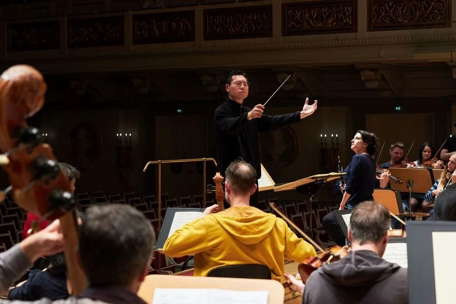 Orchestra conductor leading musicians during rehearsal in a concert hall.