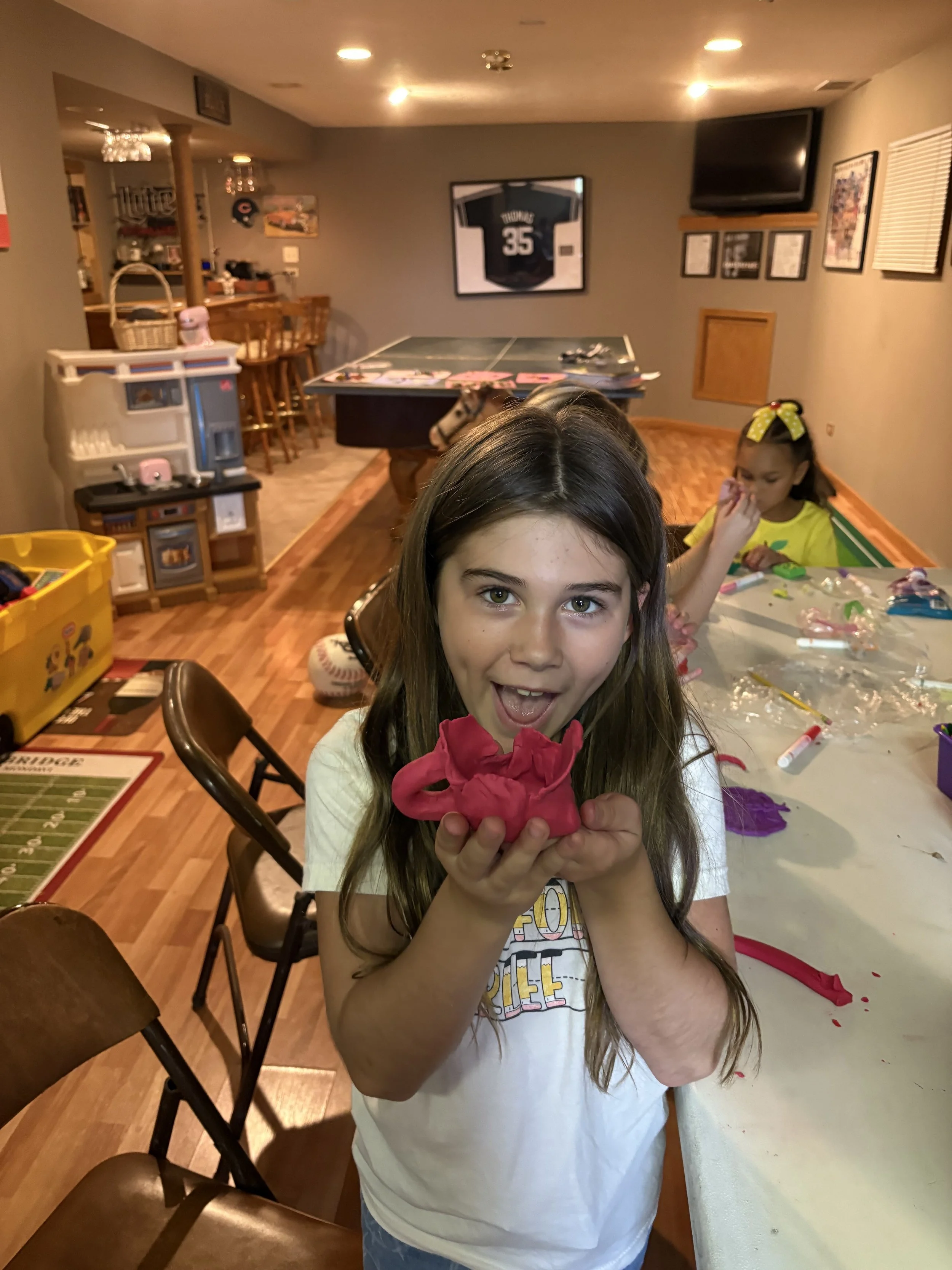 Young girl holding a pink balloon sculpture indoors at a birthday party.