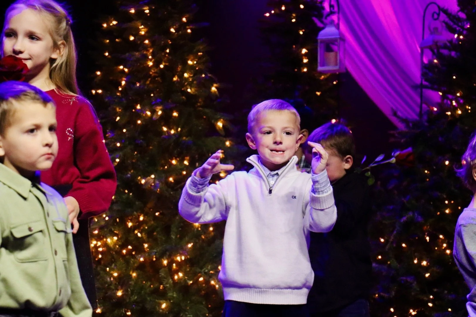 Children at a Christmas event, with decorated trees and lights in the background