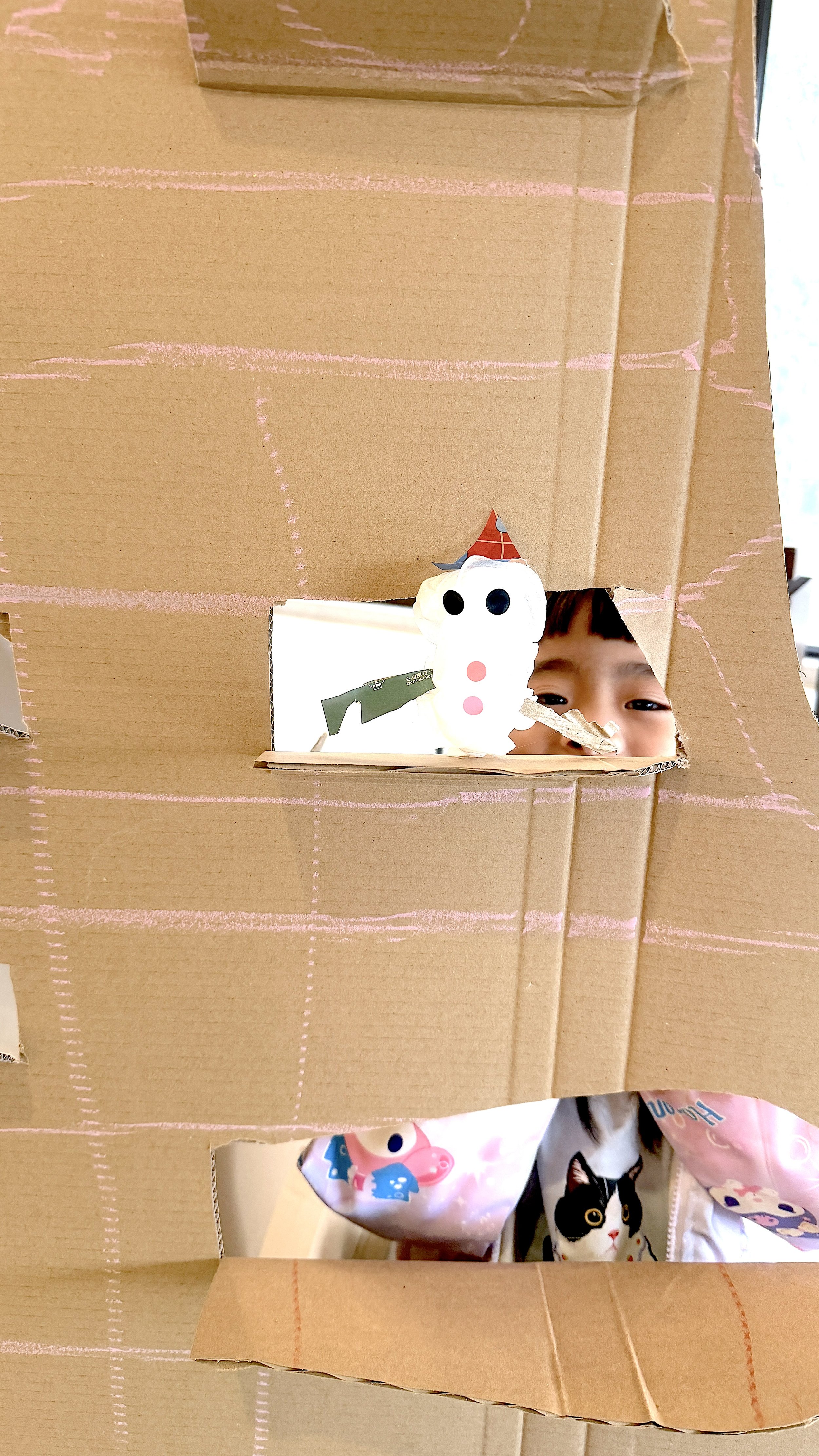 Child looking through a cardboard box with a snowman craft inside and colorful clothing with cartoon characters.
