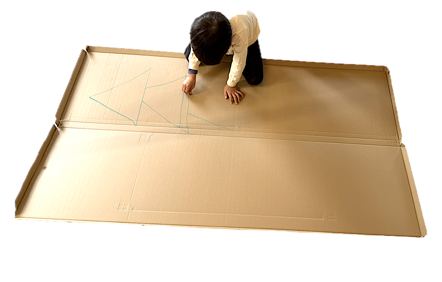Child drawing on large cardboard surface with blue marker, viewed from above.