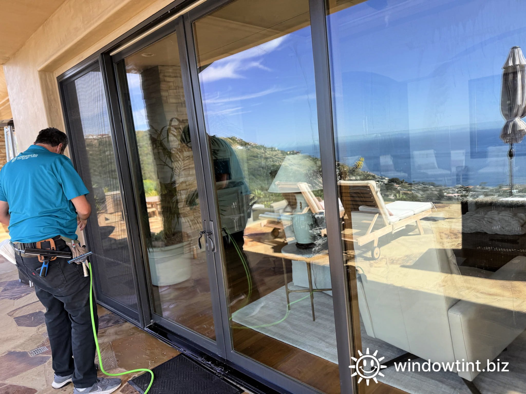 Security window film installation on large sliding glass doors in Dana Point, CA home with ocean view, technician applying film to improve safety and protect against break-ins