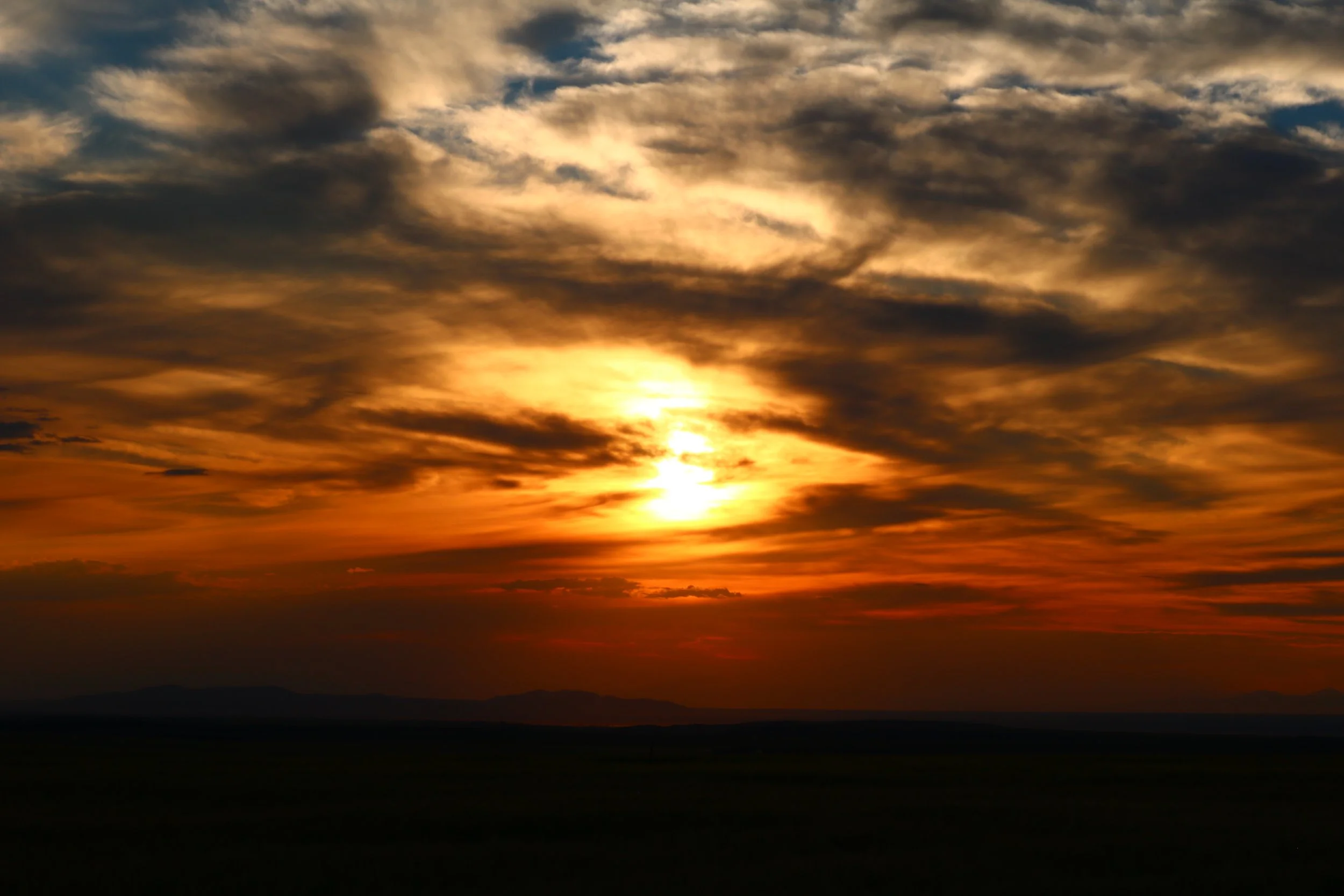 Sunset with golden orange and dark clouds over a distant landscape.