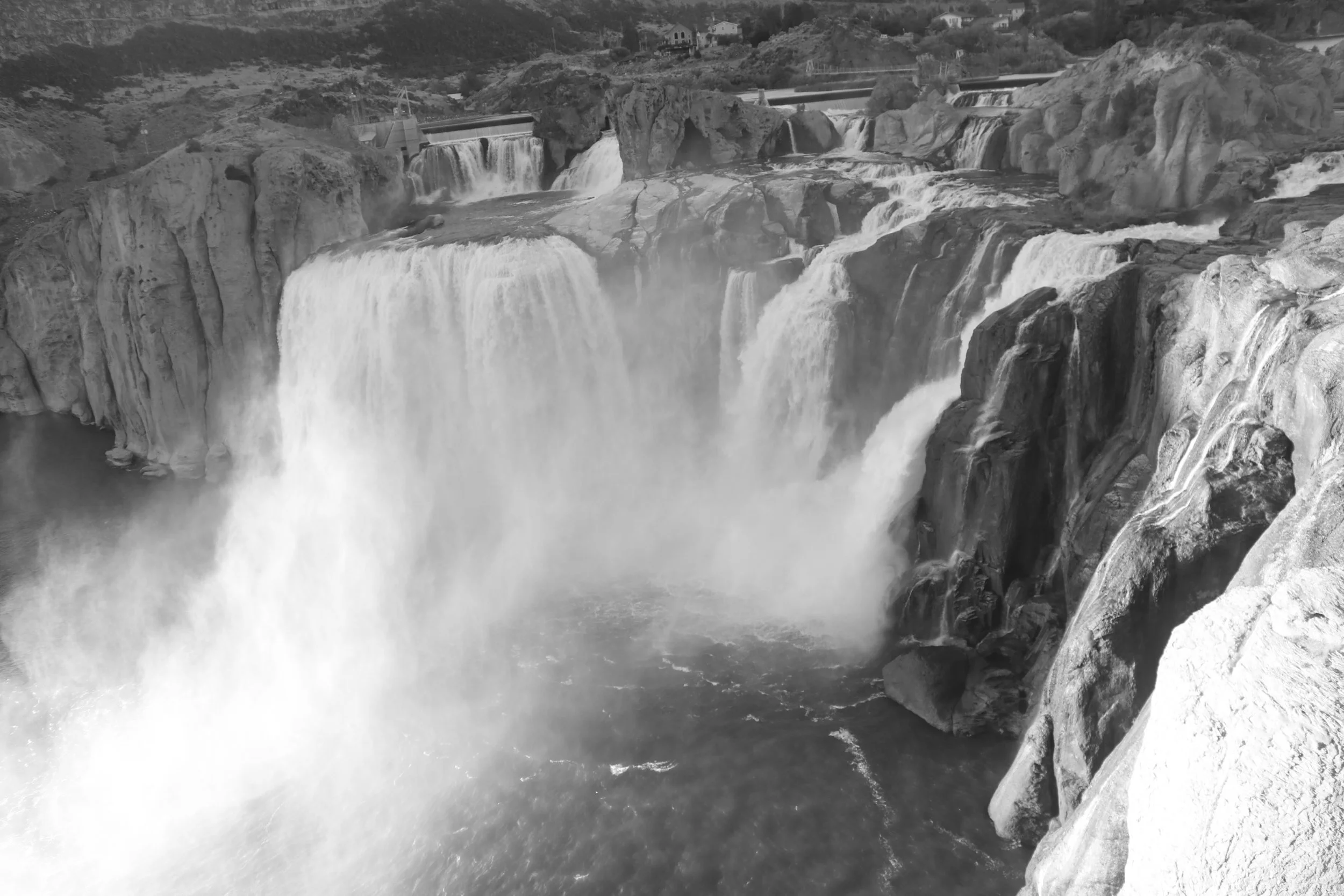 Black-and-white photo of  Shoshone waterfall cascading over rocks with a dam structure