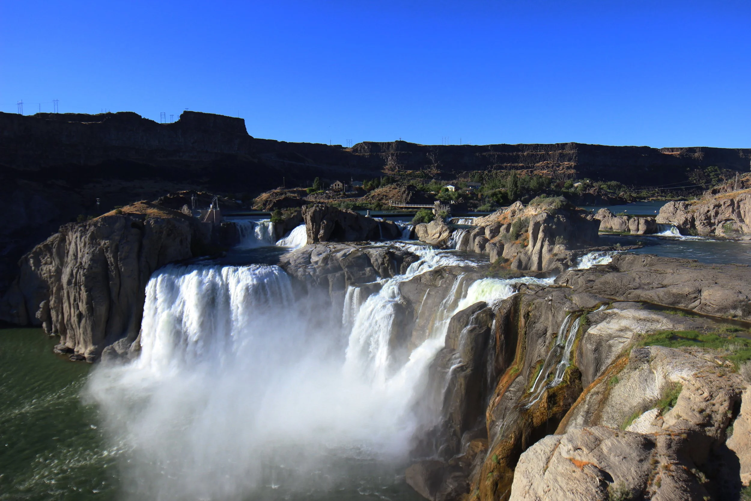 a colored photo of Shoshone Falls, a rushing waterfall cascades over a rocky terrain with a blue sky in the background