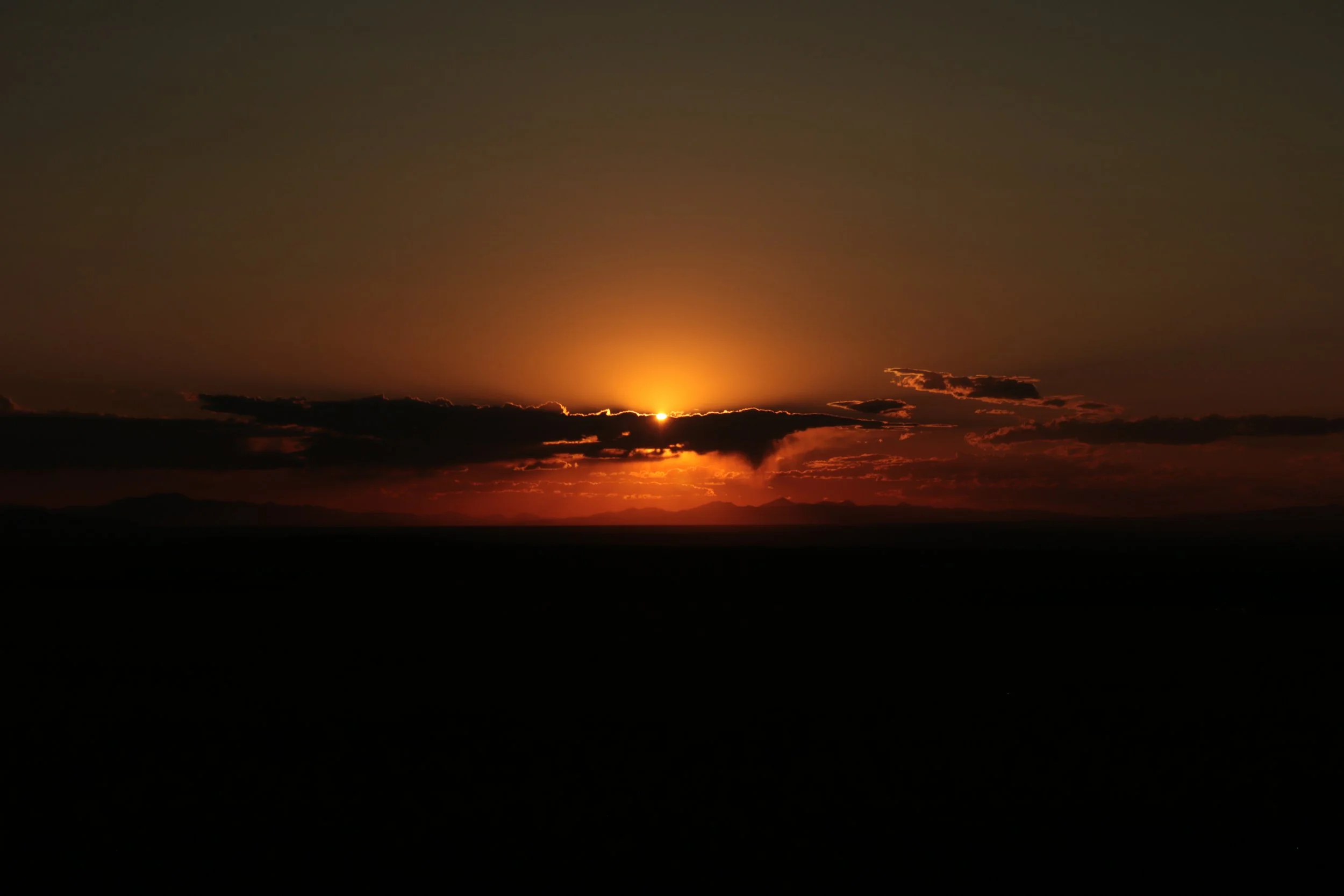Sunset over a mountainous horizon with dark clouds and a glowing orange sky.