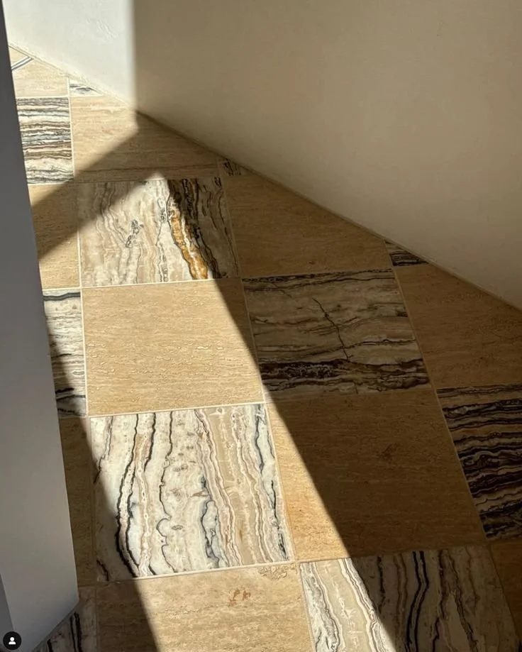 Close-up of a tiled floor with sunlight casting shadows, highlighting different patterns and colors on the tiles.