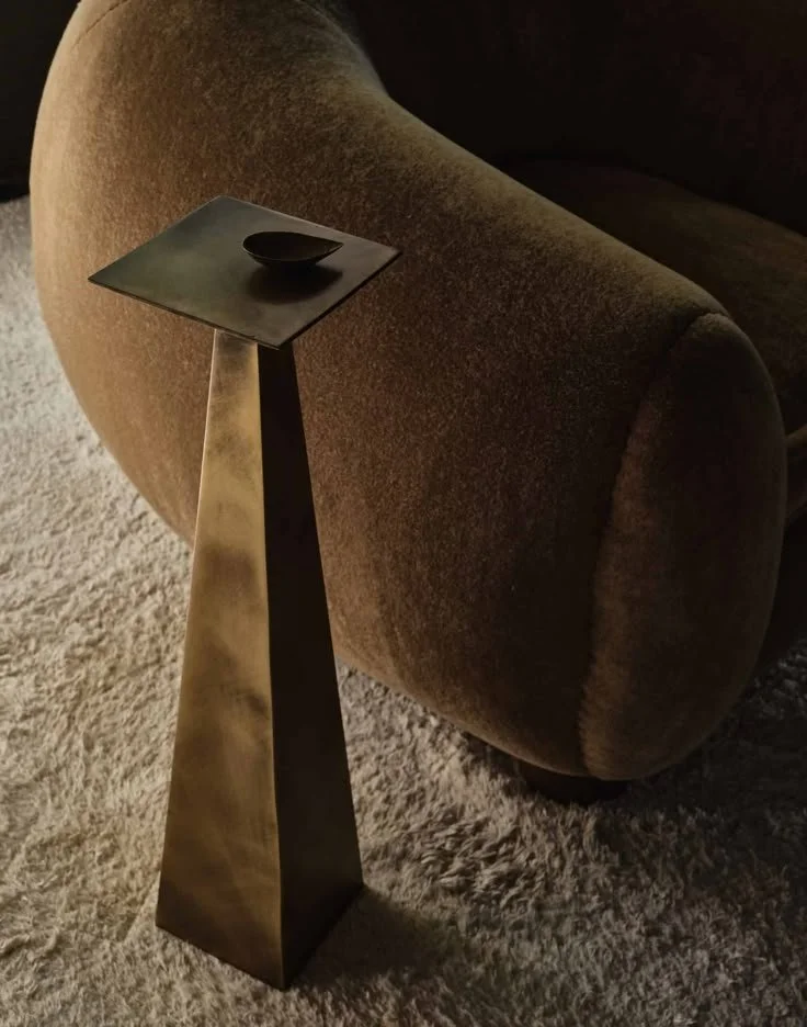 A black square side table with a small black bowl on top, next to a brown upholstered armchair on a light-colored carpet by Palooza Design.