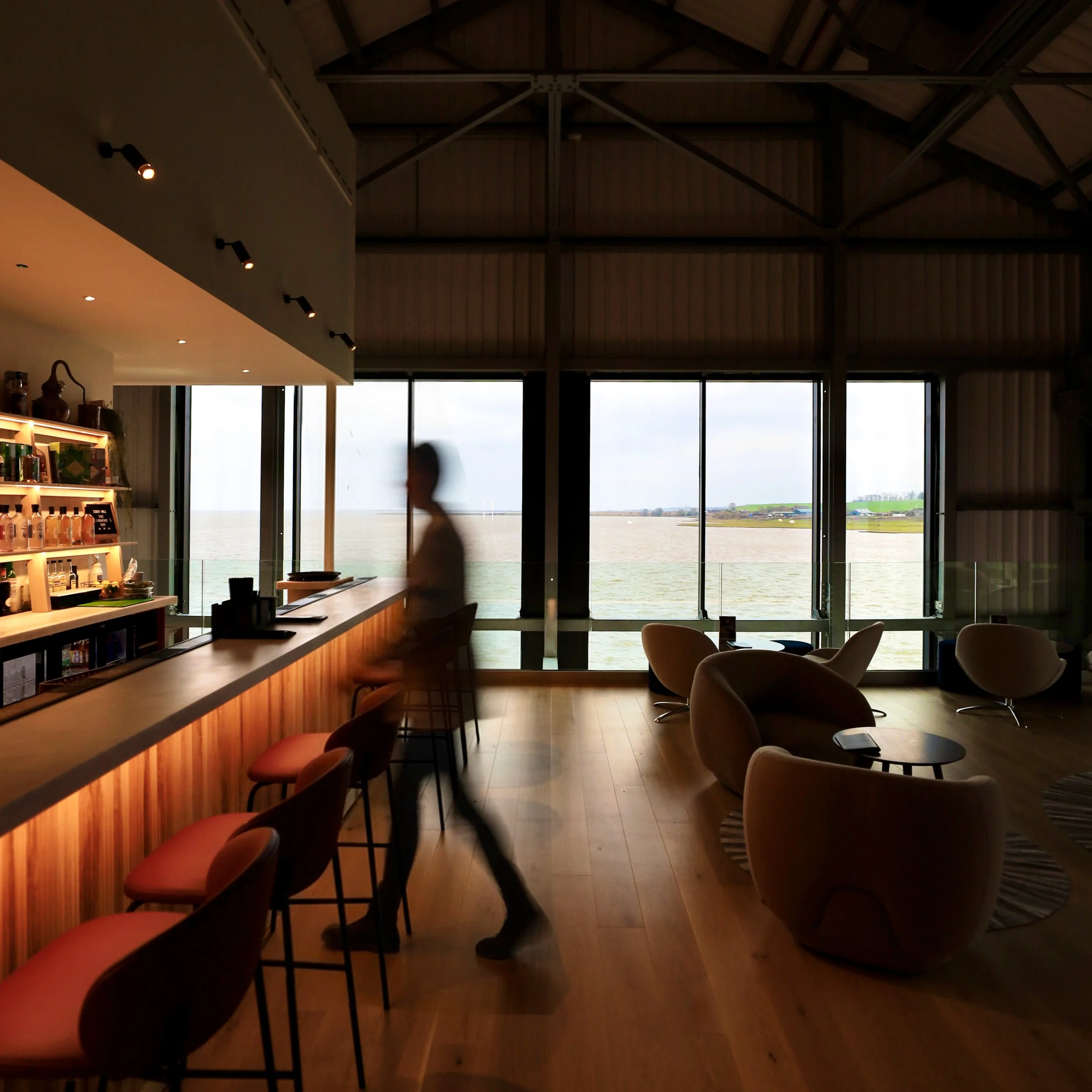 An ambiently lit bar space, with luxurious low seating and windows framing a view of the Eden Estuary