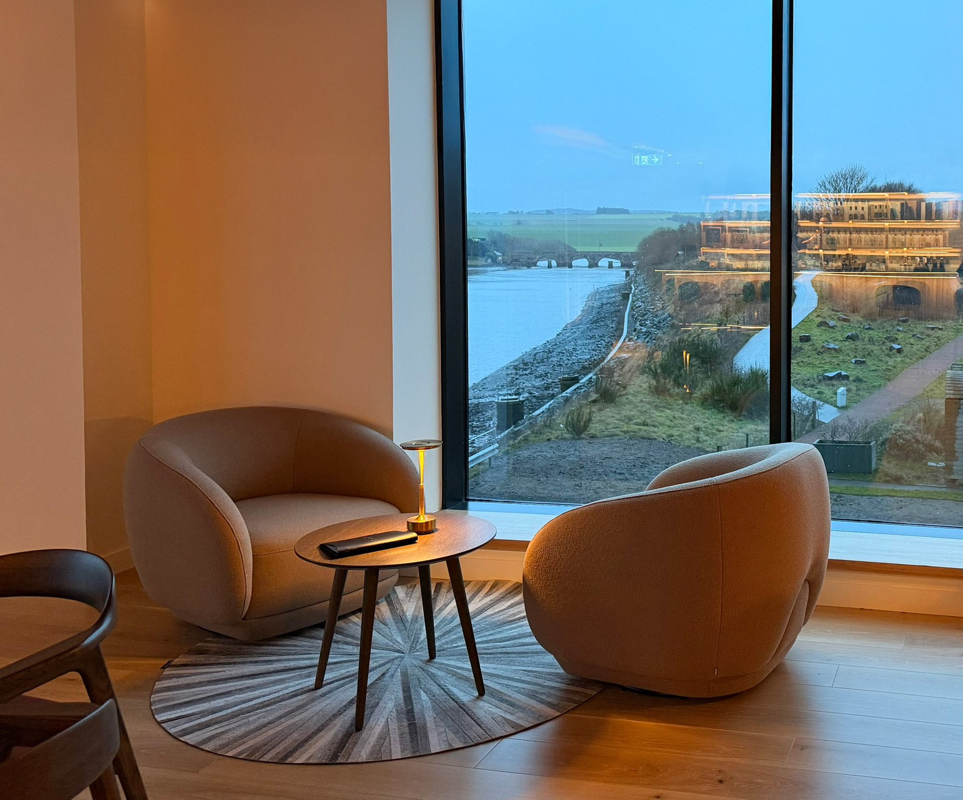 Two contemporary low armchairs positioned in front of a large window. Outside, the Eden Estuary and an old stone bridge are visible