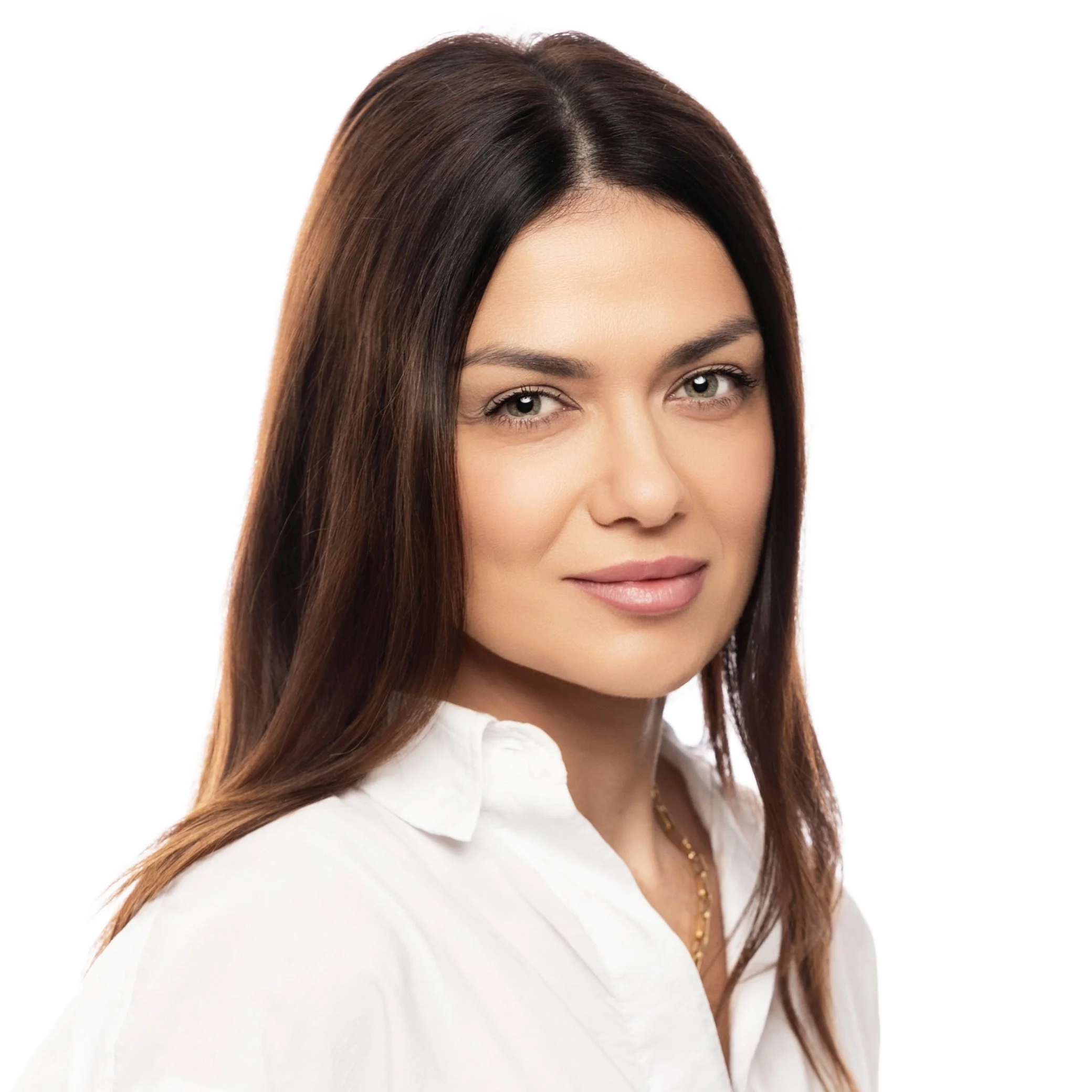 Close-up of a woman with long, brown hair, wearing a white shirt and a gold necklace, smiling softly against a plain white background.