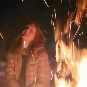 A woman smiling near a campfire at night.