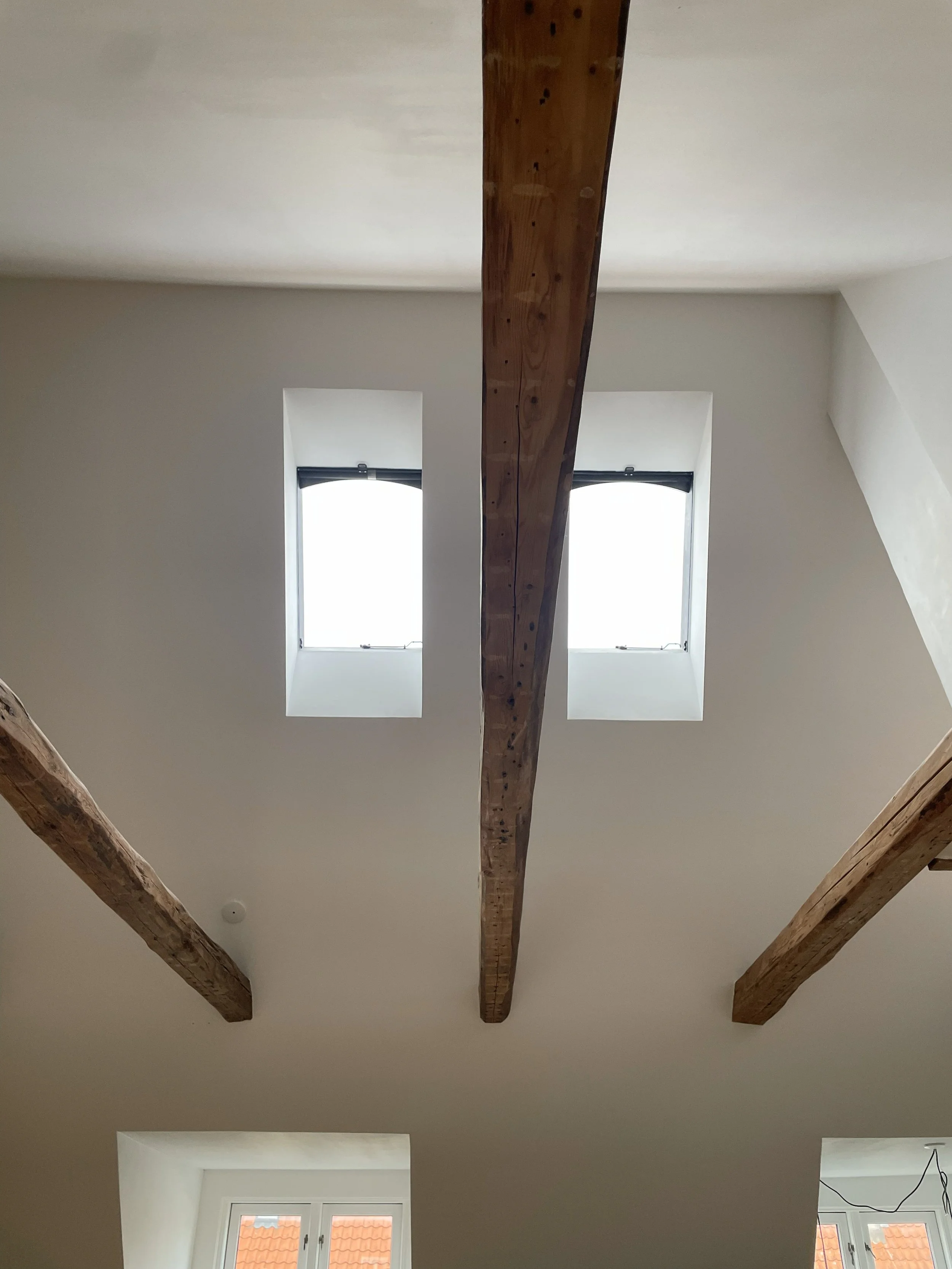 Ceiling view of a room with exposed wooden beams and two skylight windows.