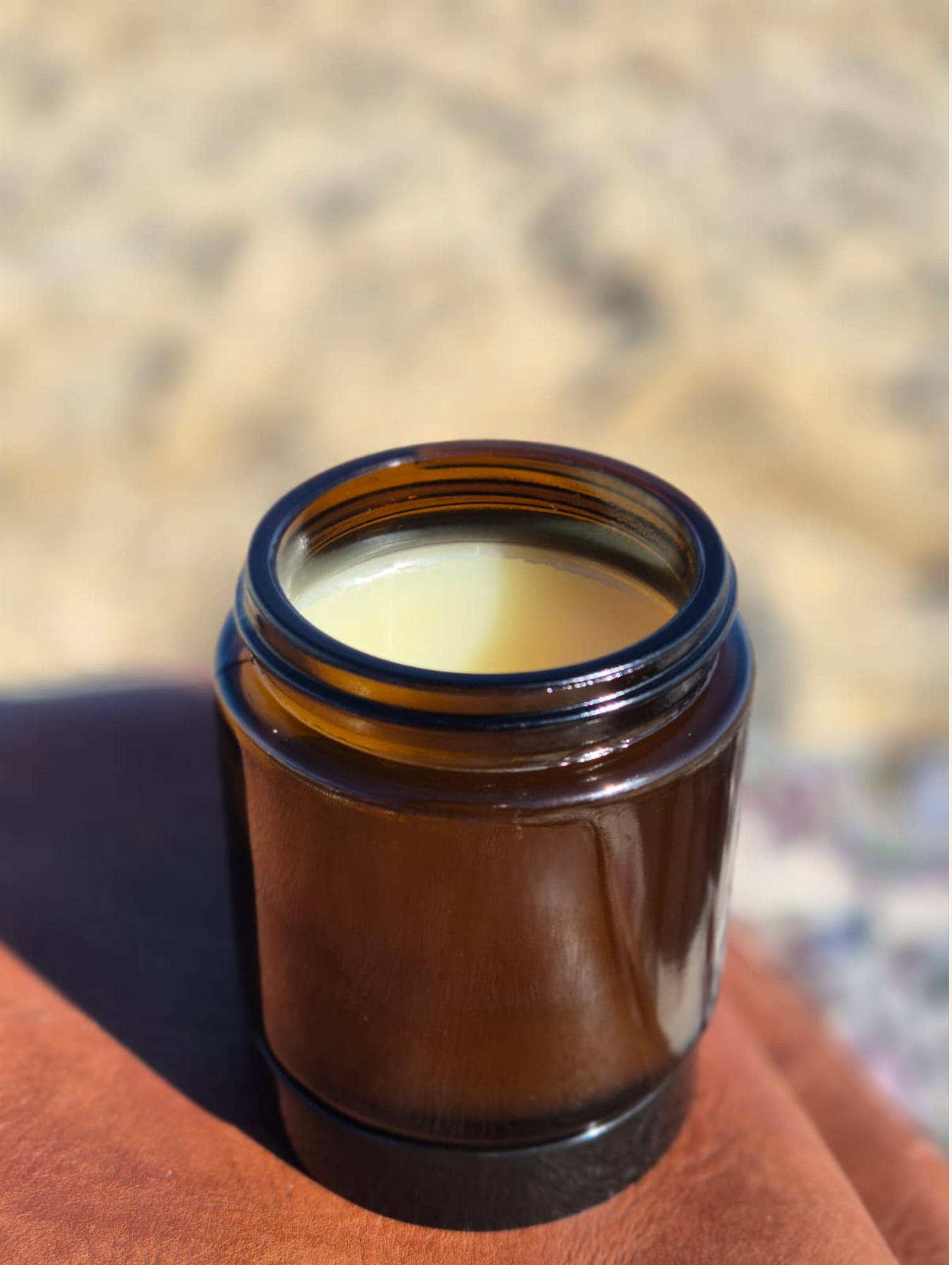 An open amber glass bottle containing a light-colored liquid, placed on a wooden surface with a black object nearby.