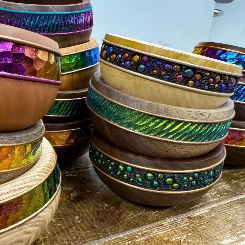 Stacked wooden bowls decorated with colorful, glittery, and textured patterns.