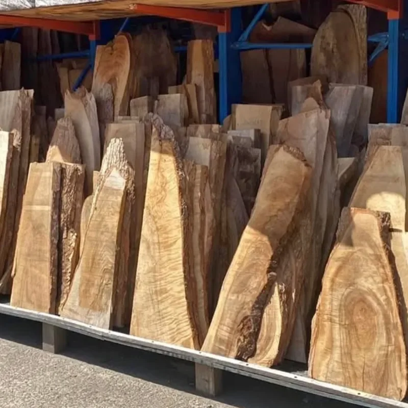 Stacked slabs of wood stored on a rack, with some pieces showing natural edges and grain patterns.