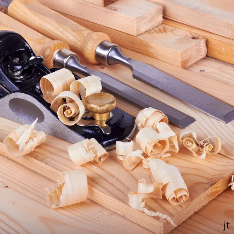 Woodworking tools including a hand plane, chisels, and clamps on a wooden surface, with wood shavings scattered around.
