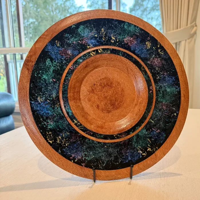 Decorative wooden plate with colorful scientific-like pattern on the outer ring, displayed on a stand indoors.