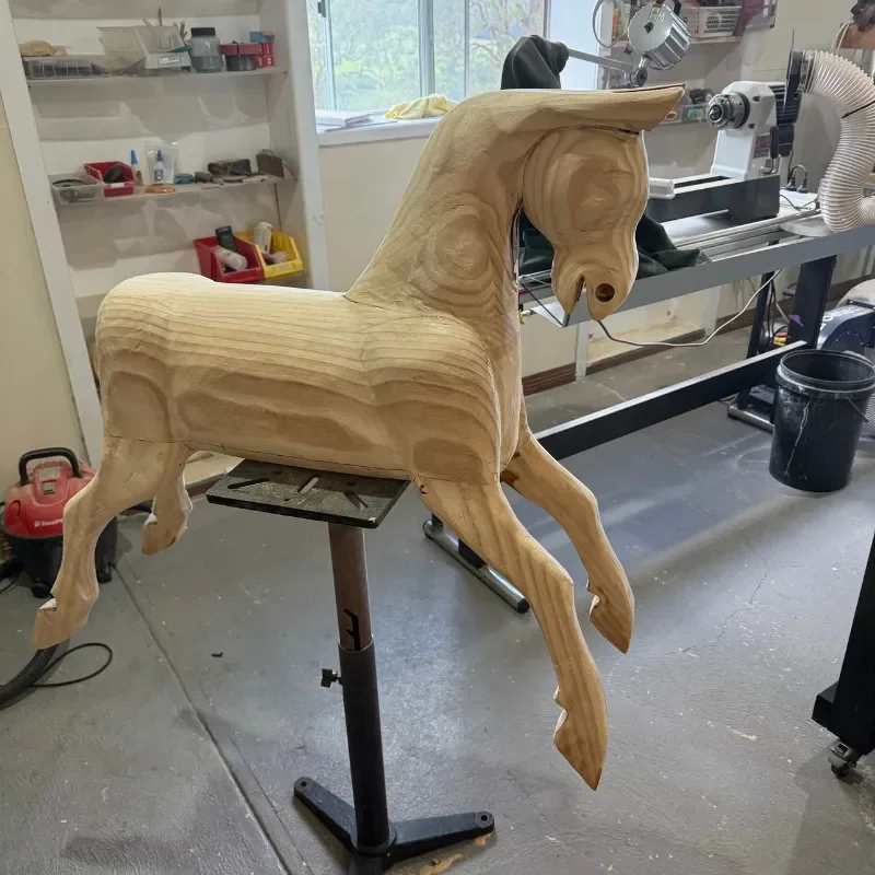 Wooden horse sculpture in a woodworking shop, on a workbench with woodworking tools and a window in the background.