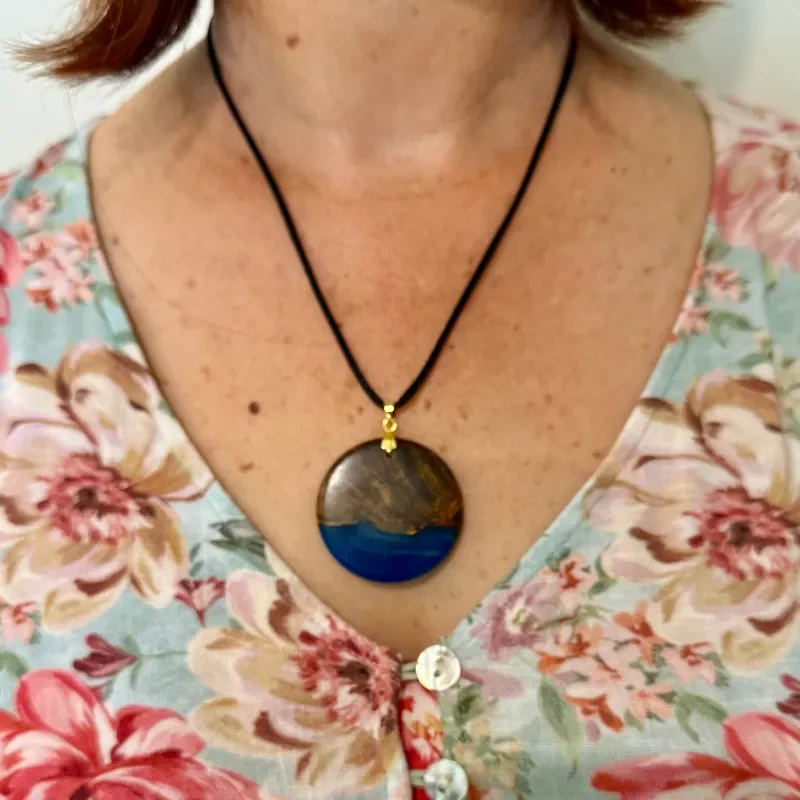 Close-up of a woman wearing a floral dress with pink, cream, and green colors, and a large, round pendant necklace with a blue and brown design.