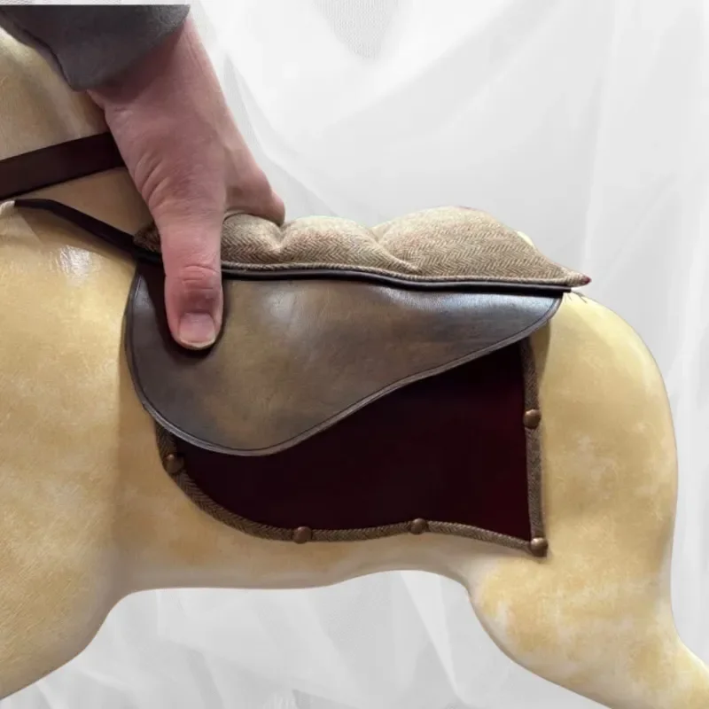 Close-up of a person flipping an equestrian saddle over a horse mannequin to show the underside.