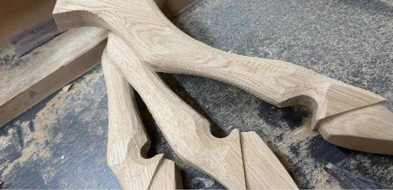 Unfinished carved wooden piece with intricate design, resting on a work surface covered in sawdust.