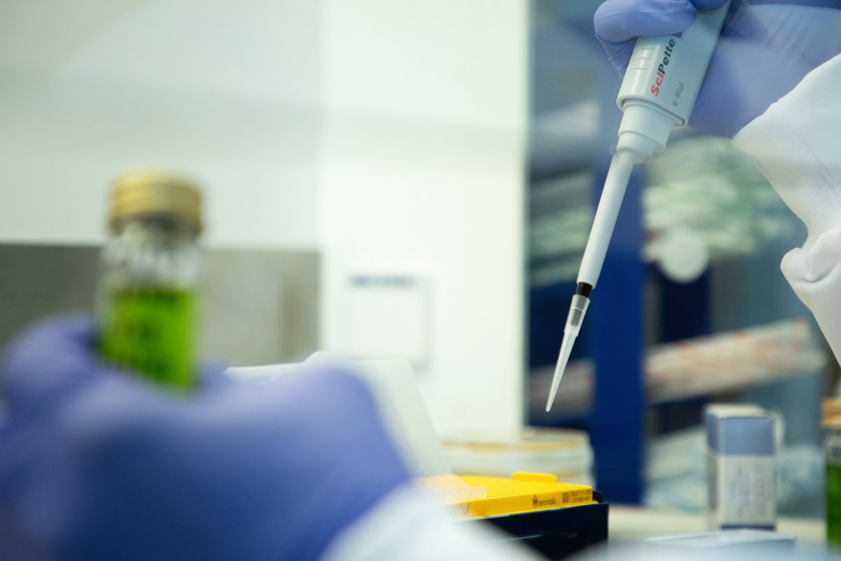 A scientist using a pipette to transfer liquid into a container in the Axitan laboratory setting.