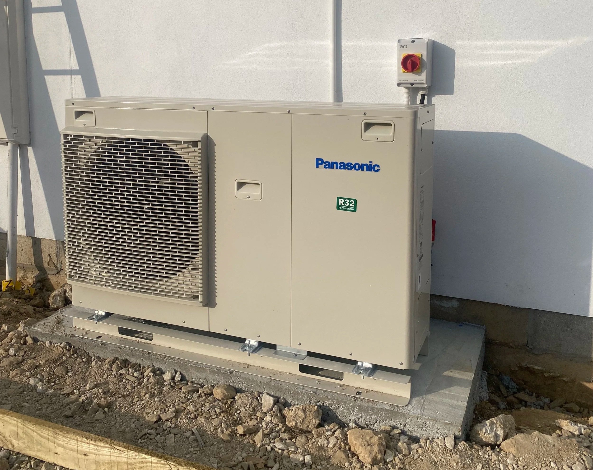 Outside view of a Panasonic HVAC unit with a red power switch mounted on a white wall installation.