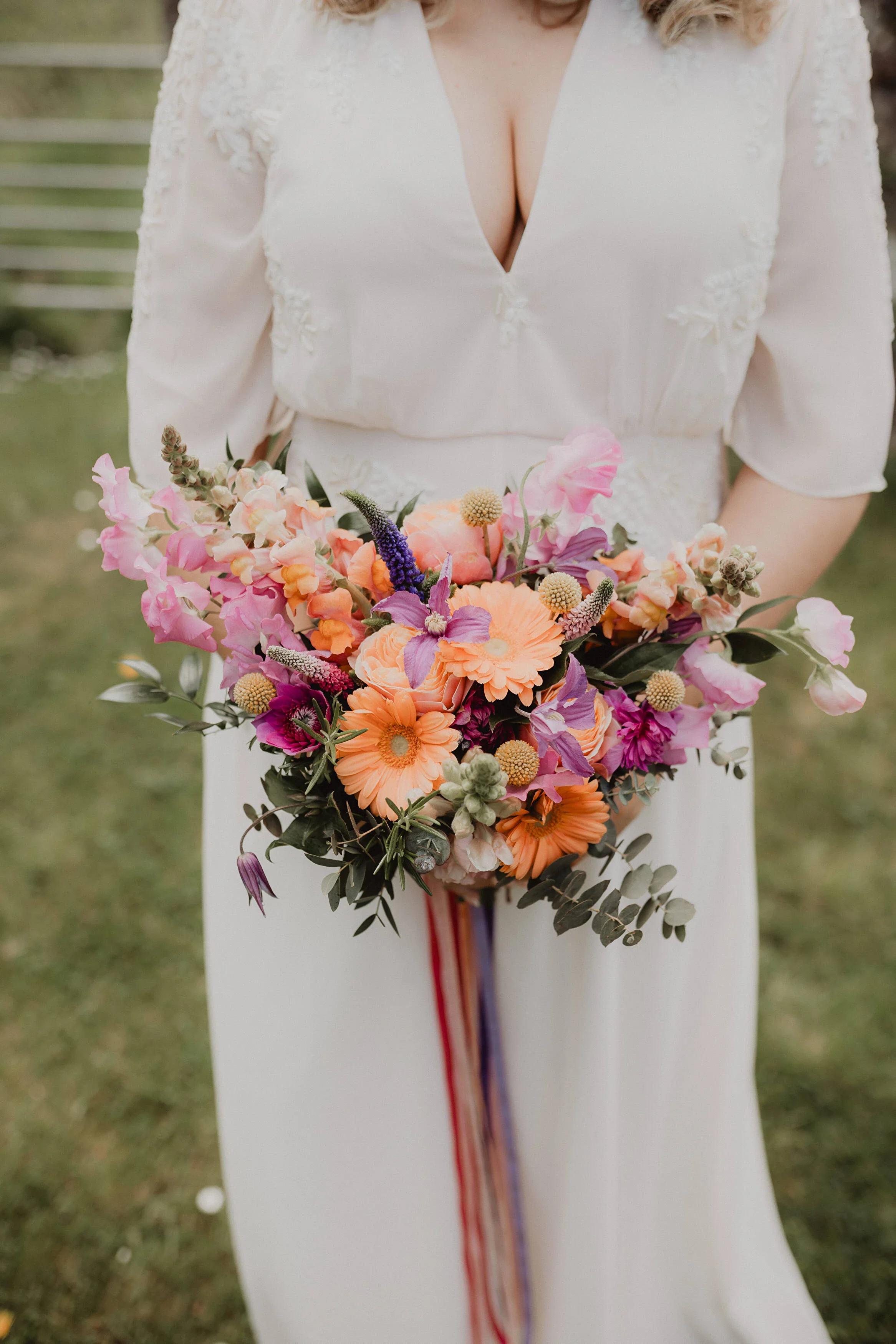 A woman in a white dress holding a colorful bouquet of flowers outdoors.