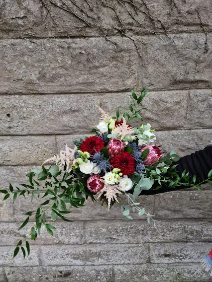 Person holding a colorful bouquet of flowers in front of a brick wall.