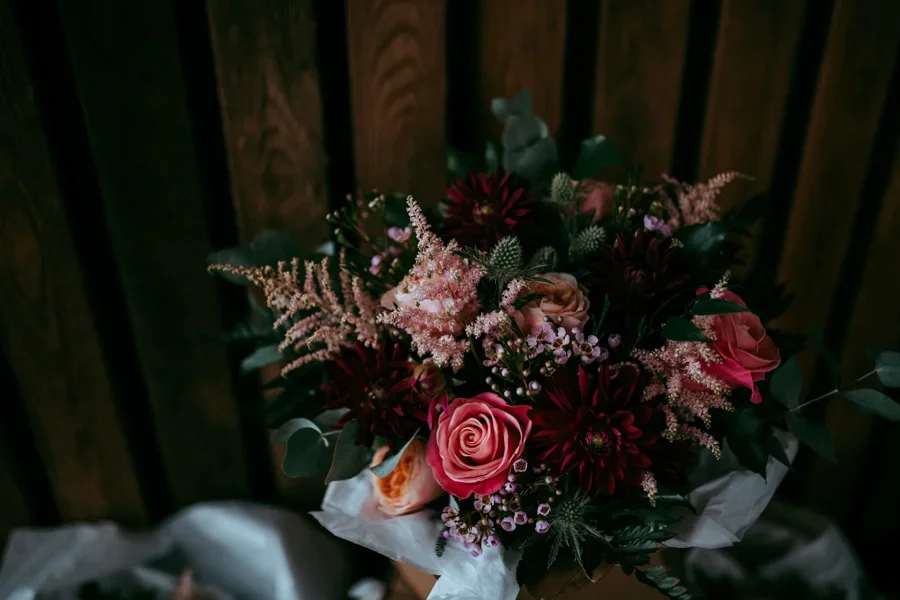 A bouquet of pink roses, dark red dahlias, and pink astilbe with greenery on a wooden surface.
