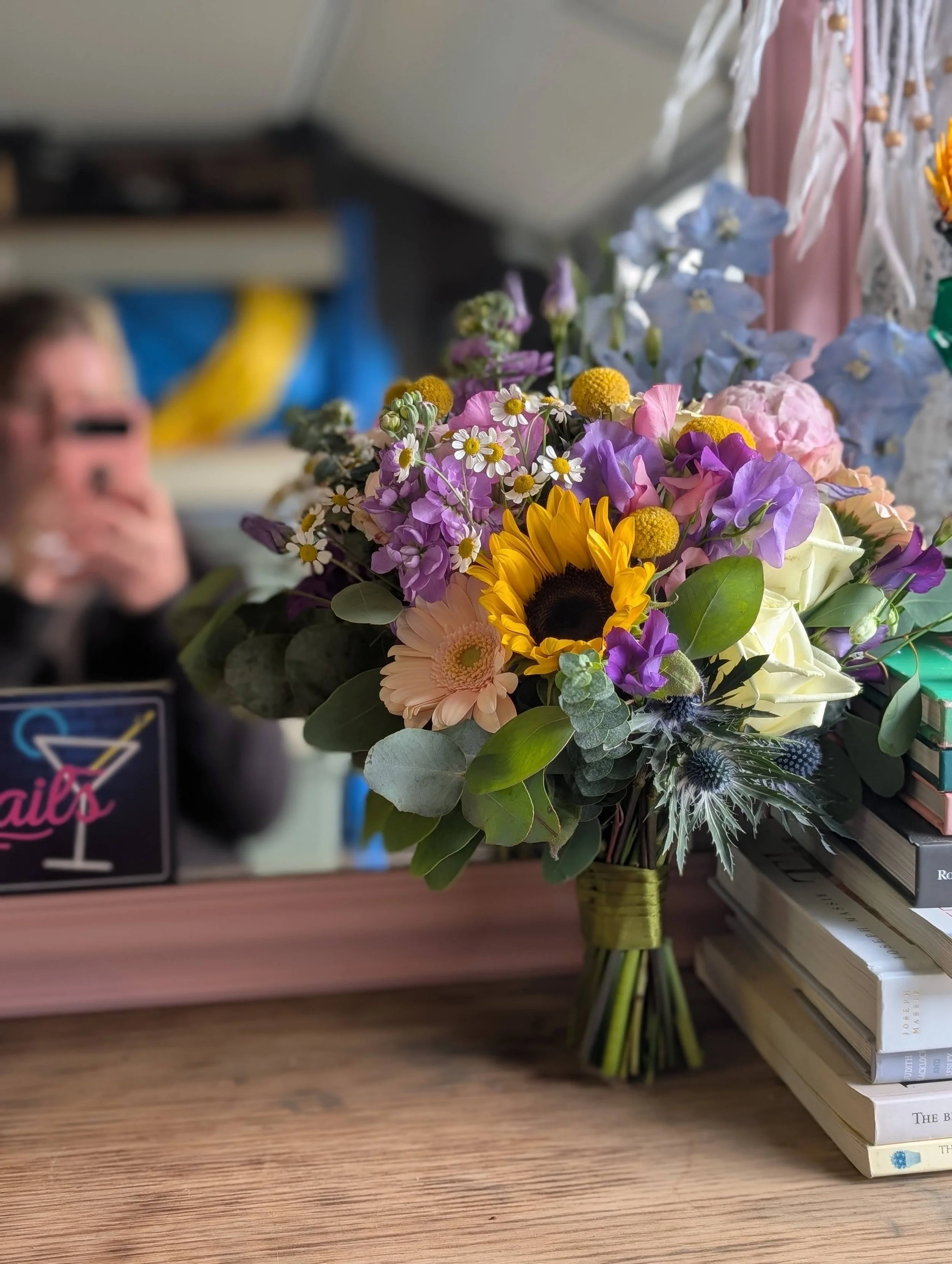 Brightly colored bouquet of flowers including sunflowers, daisies, and other mixed flowers on a table.