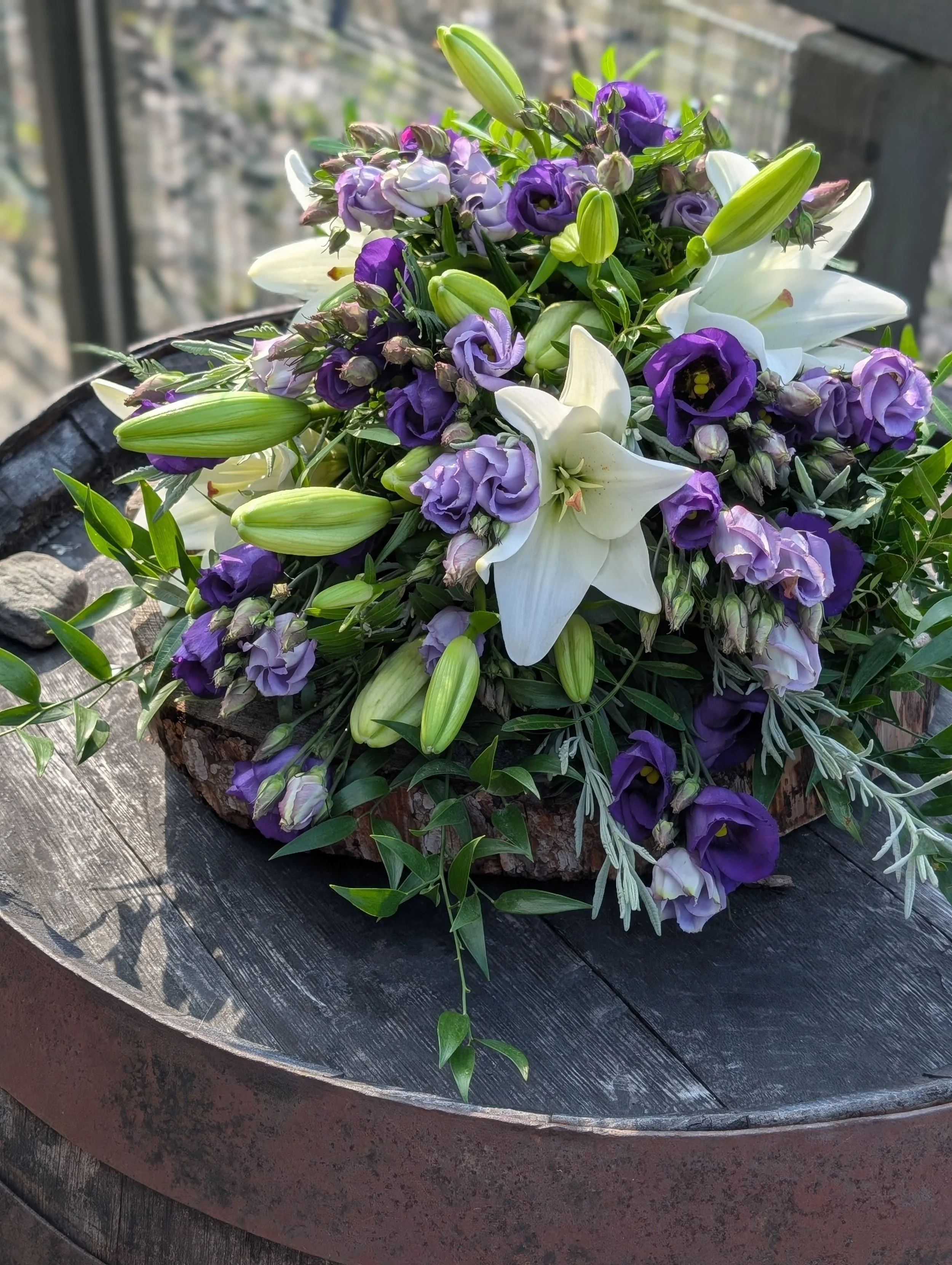 A floral arrangement with white lilies and purple flowers on a wooden surface.