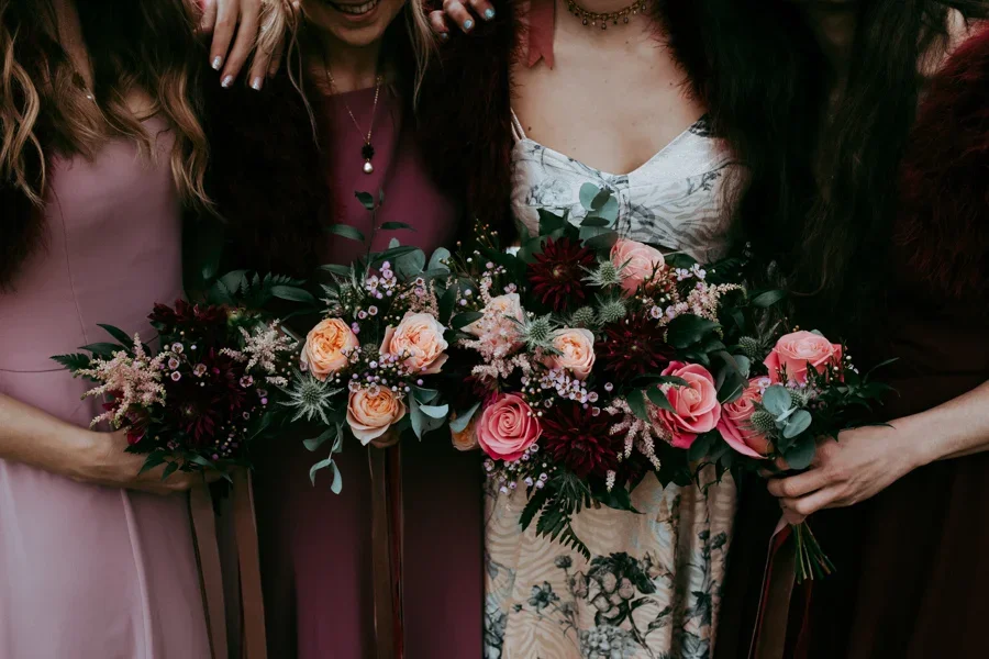 Three women holding floral bouquets, dressed in stylish dresses, at a celebration or event.