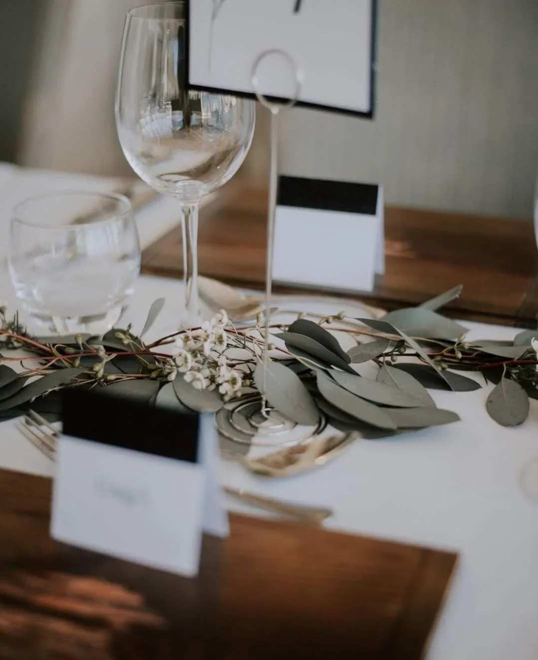 Elegant table setting with wine glasses, a small floral arrangement, and place cards.