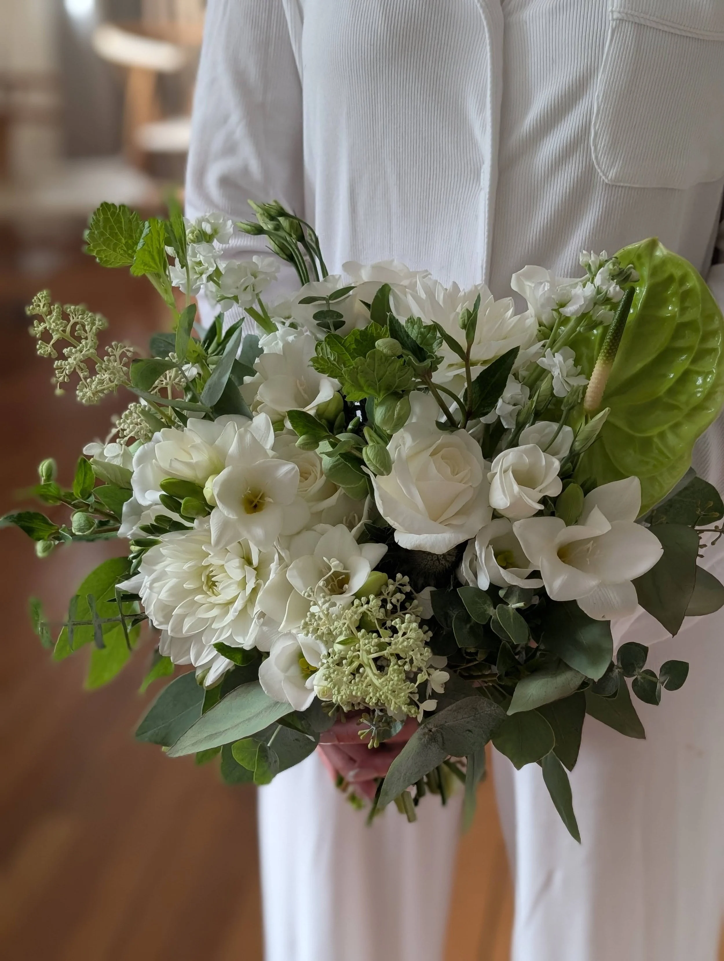 Person holding a bouquet of white flowers and green foliage.