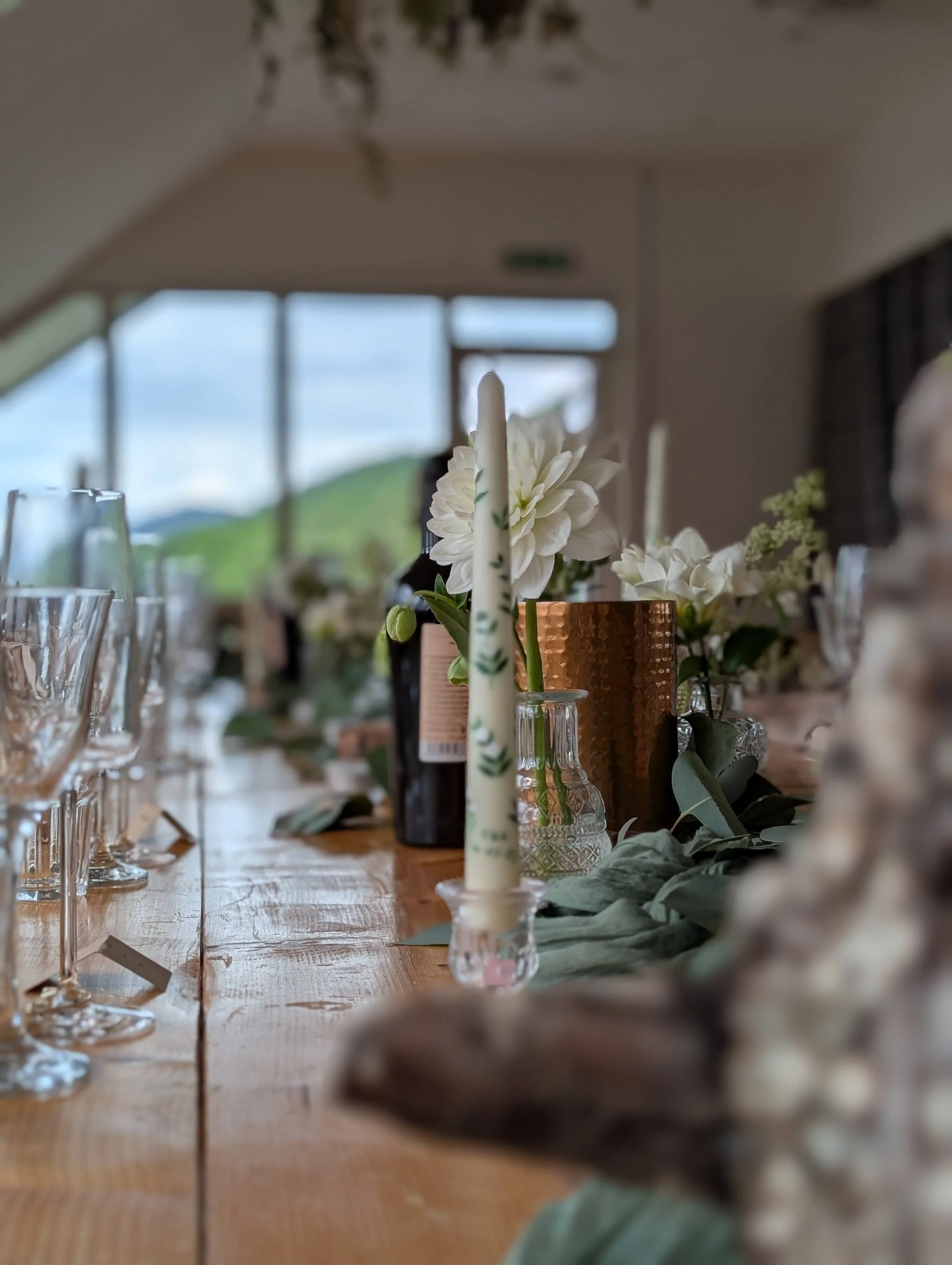 A decorated dining table with candles, glassware, and floral arrangements with a background view of mountains and sky.