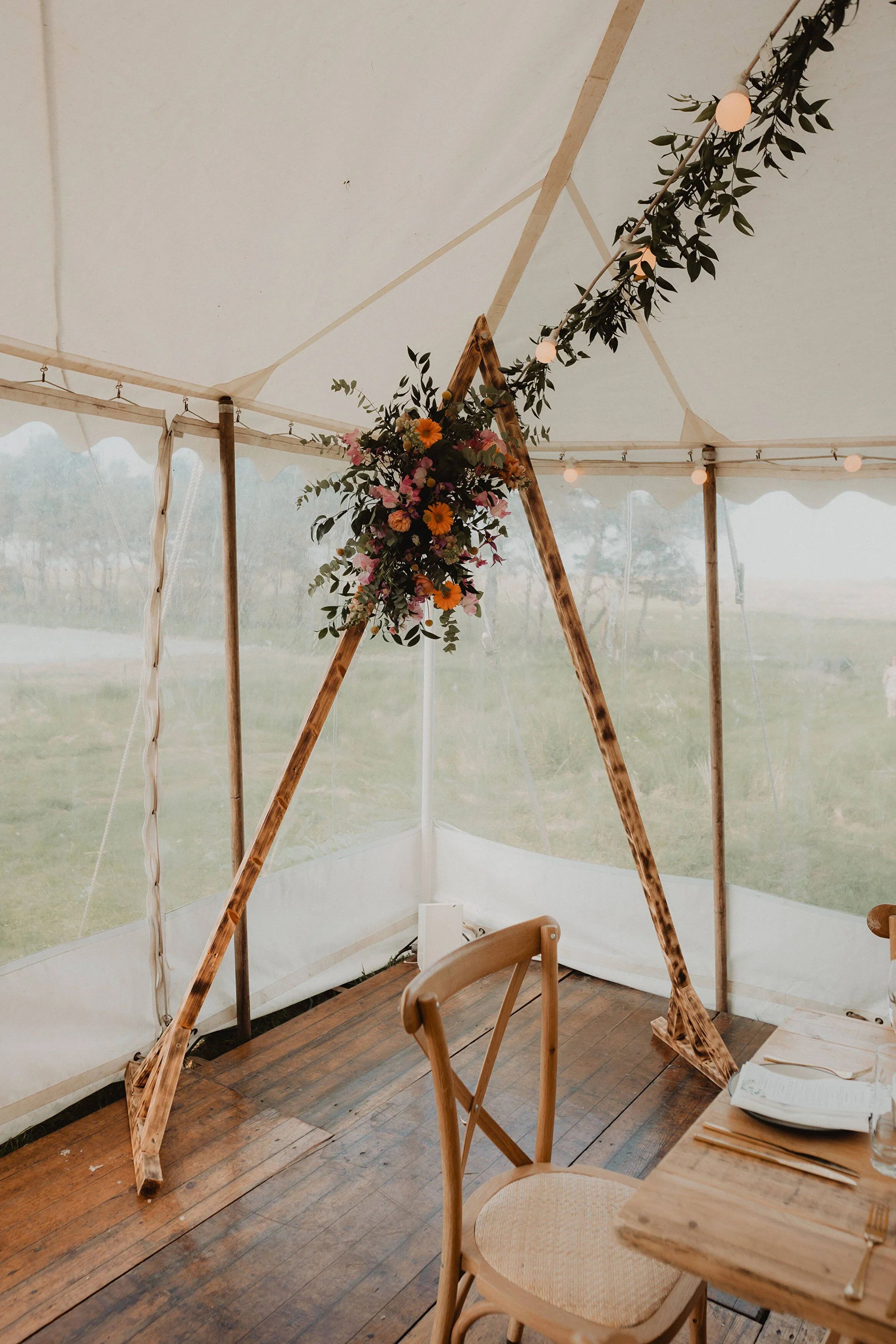 Decorative wooden arch with a floral arrangement in an event tent with string lights.