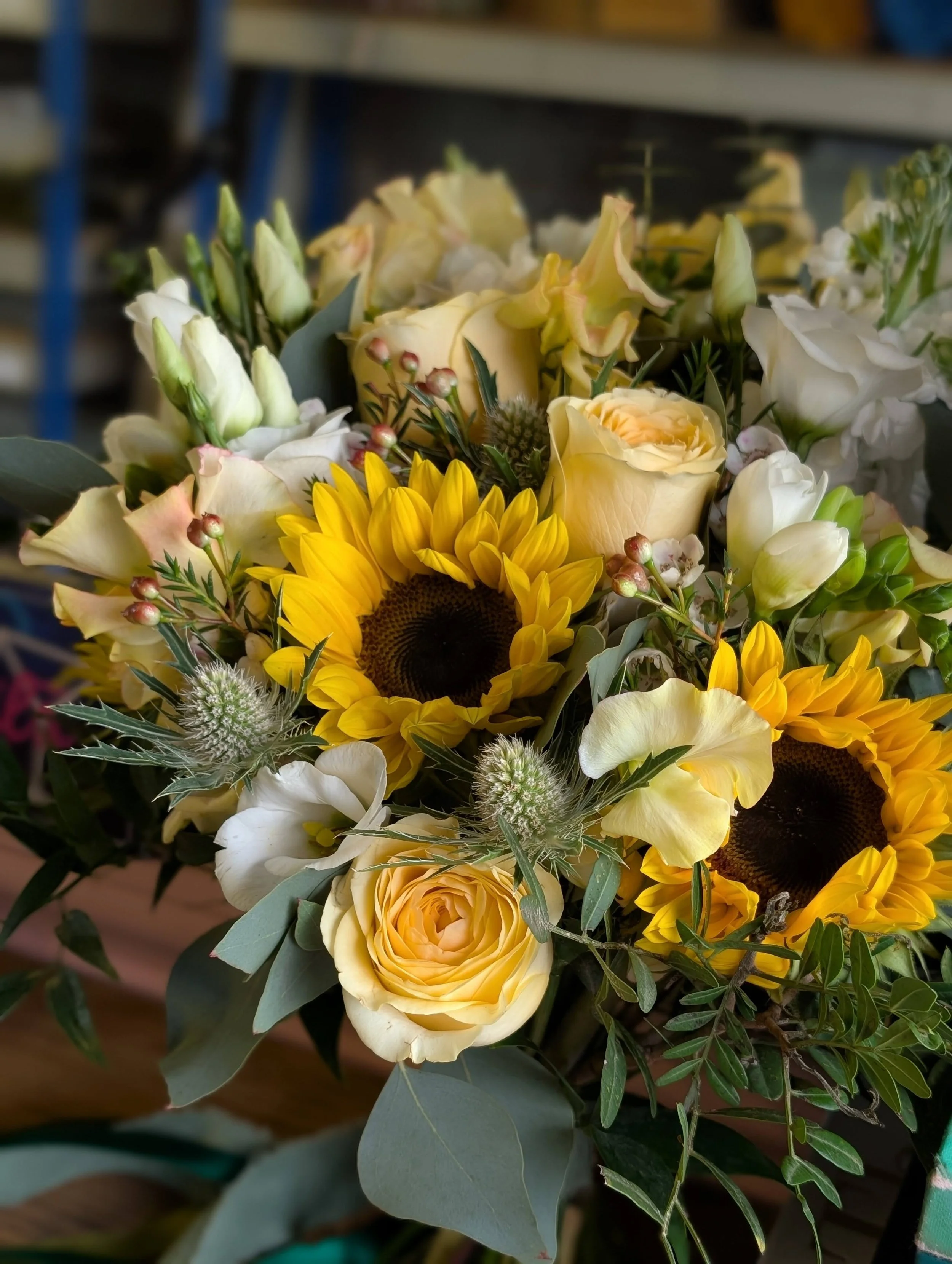 A bouquet of flowers including yellow sunflowers, white roses, white lilies, and greenery.