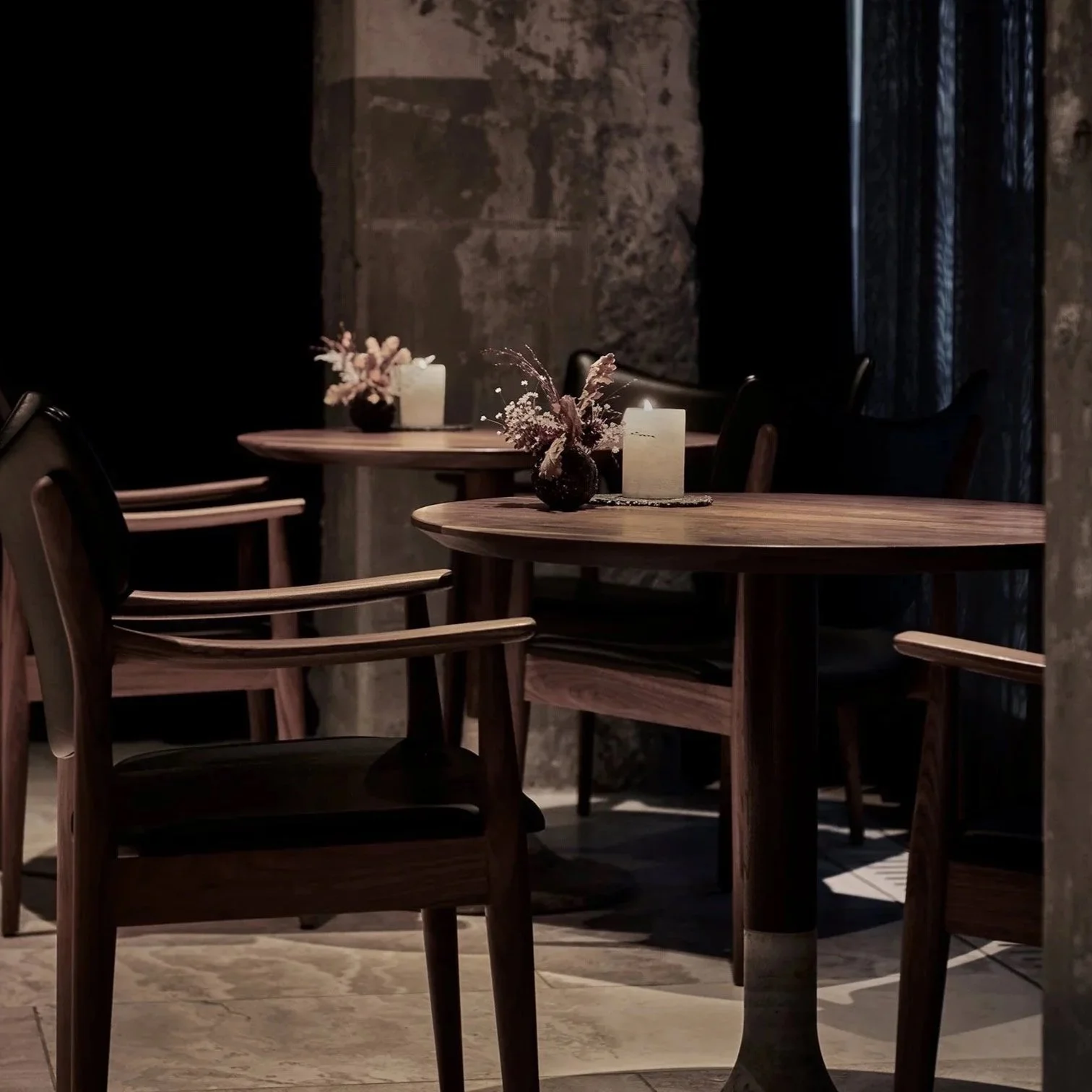 A dimly lit restaurant interior with wooden tables and chairs, decorated with candles and small flower arrangements.