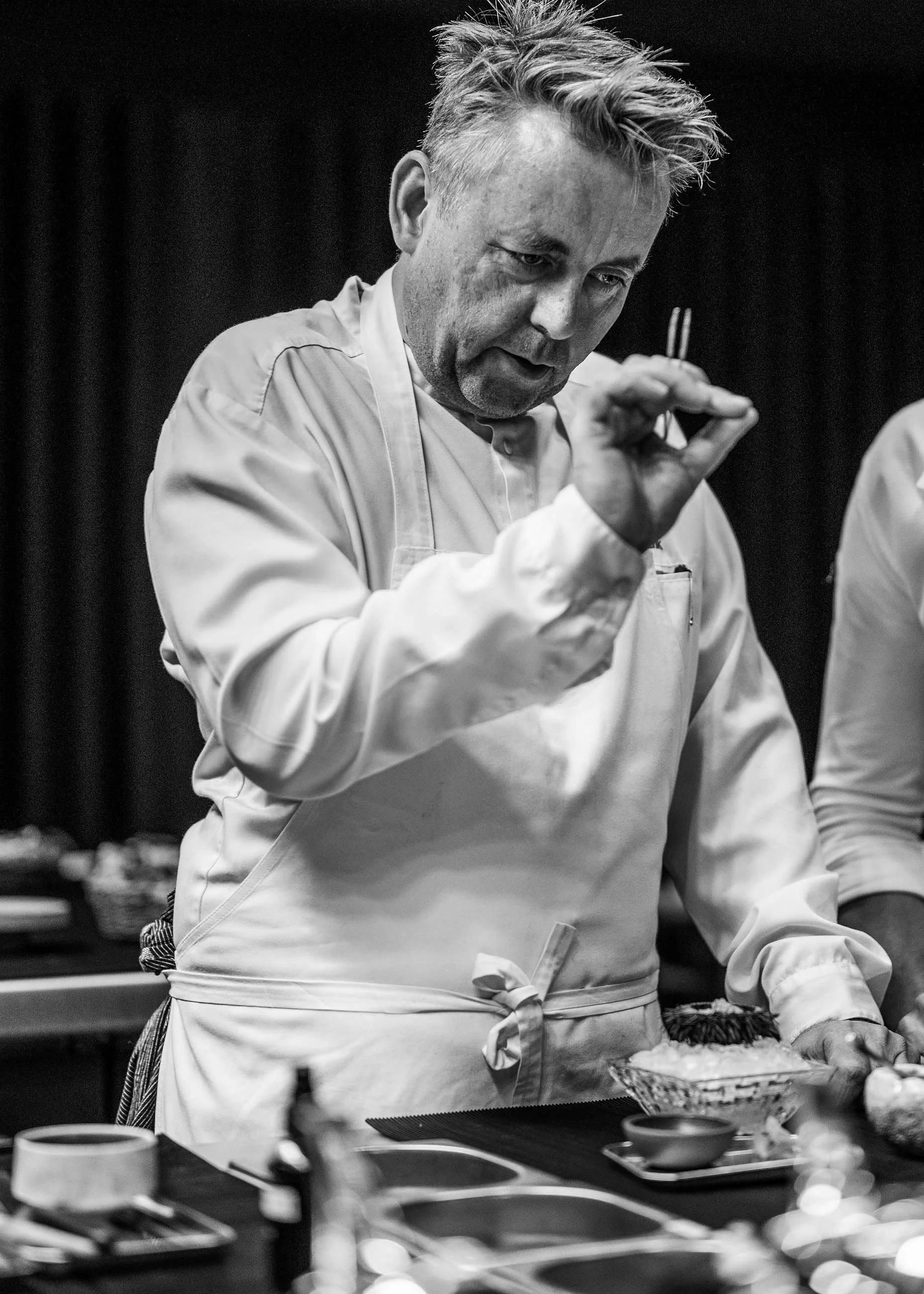 A male chef in a white apron preparing food in a kitchen.