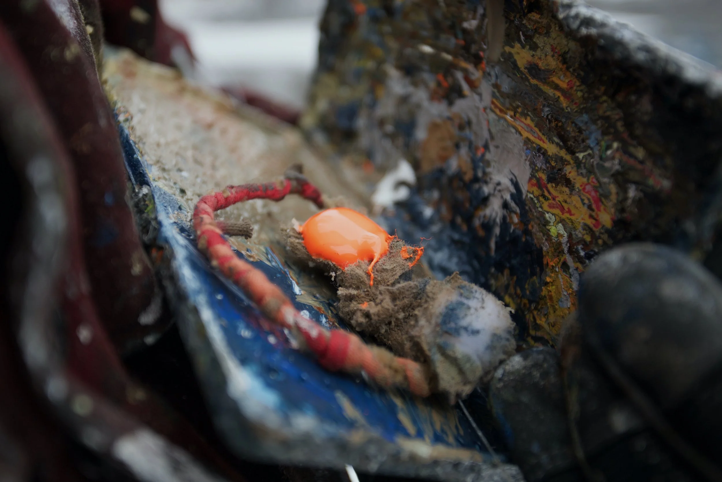 Close-up of a broken orange egg shell on a surface with dirt and debris, surrounded by peeling painted surfaces and worn materials.