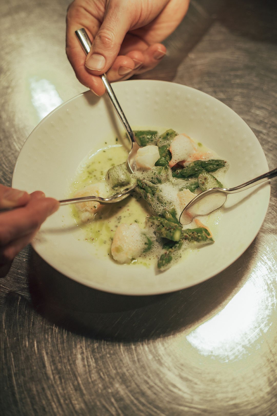 Three hands helping themselves to langoustines and asparagus on a plate.