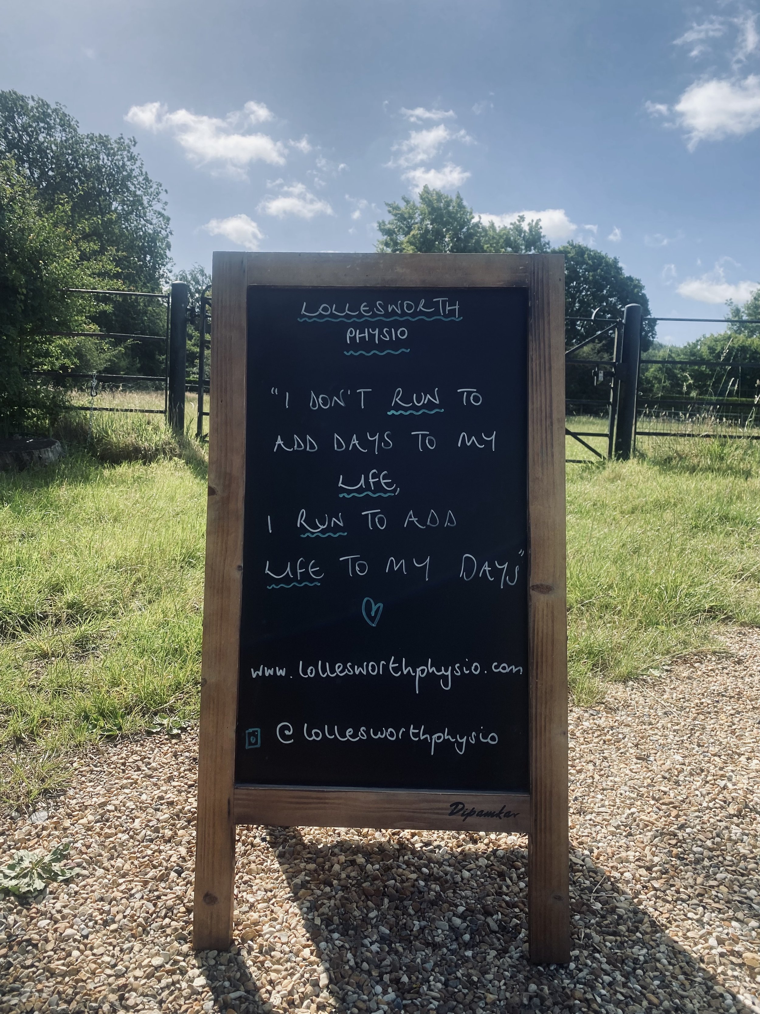 Outdoor chalkboard sign with motivational quote, surrounded by green trees under a partly cloudy sky, with a gravel surface in front. Horsely, Surrey.