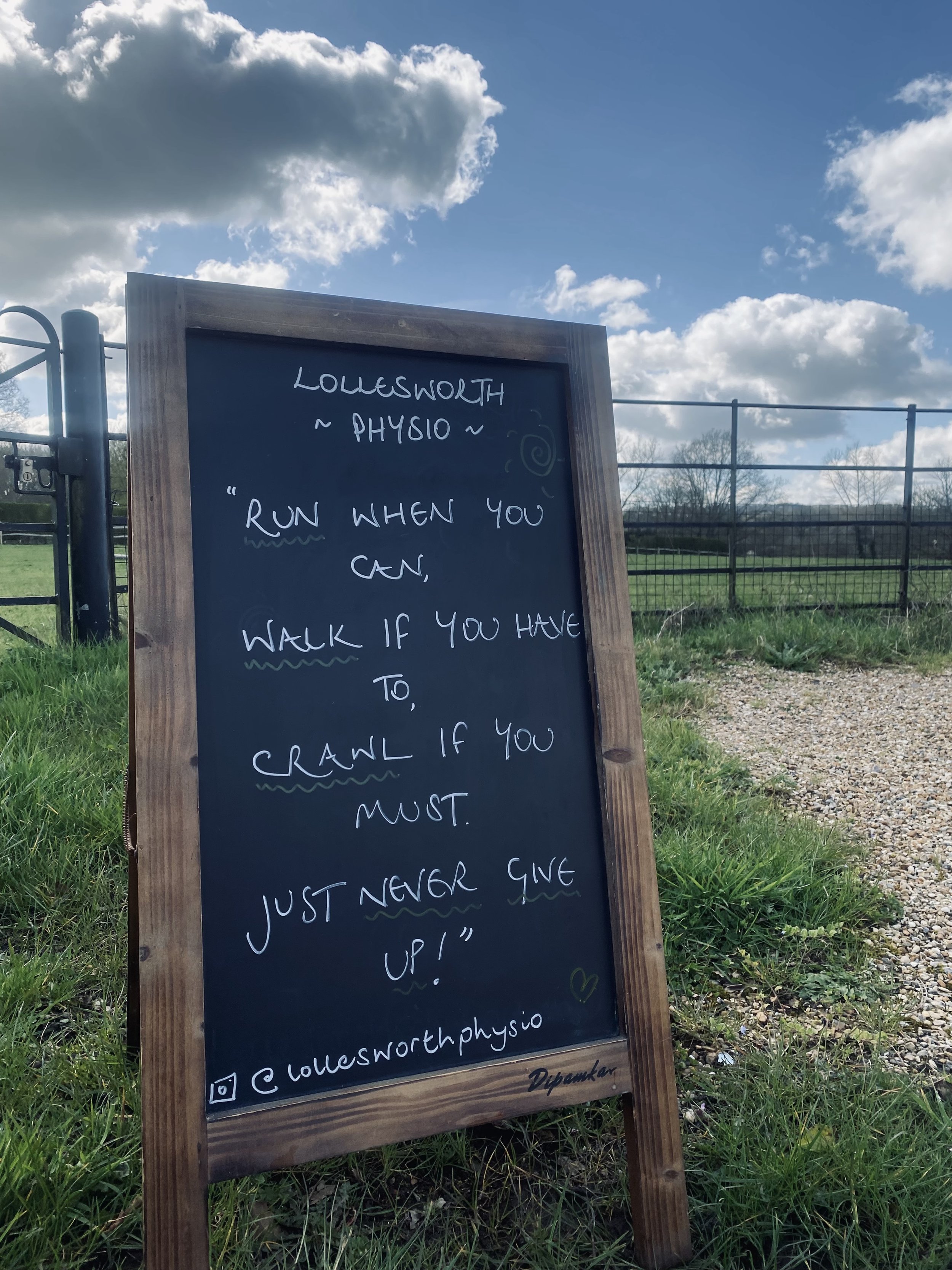 Chalkboard sign on Lollesworth Lane with motivational quote about running and walking, positioned near a grassy area with a black metal gate behind it, under a partly cloudy sky. Horsely, Surrey.