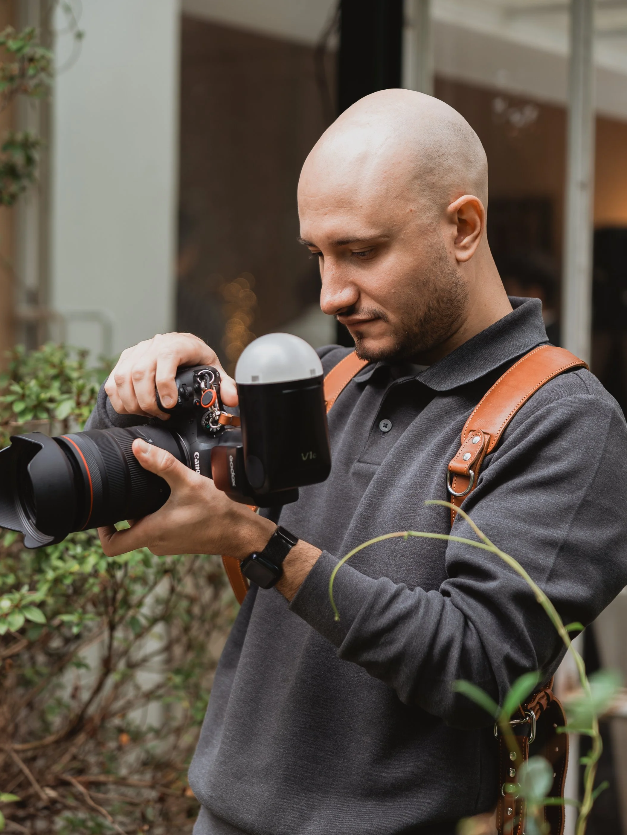 Uomo con testa rasa che controlla una fotocamera professionale all'aperto.