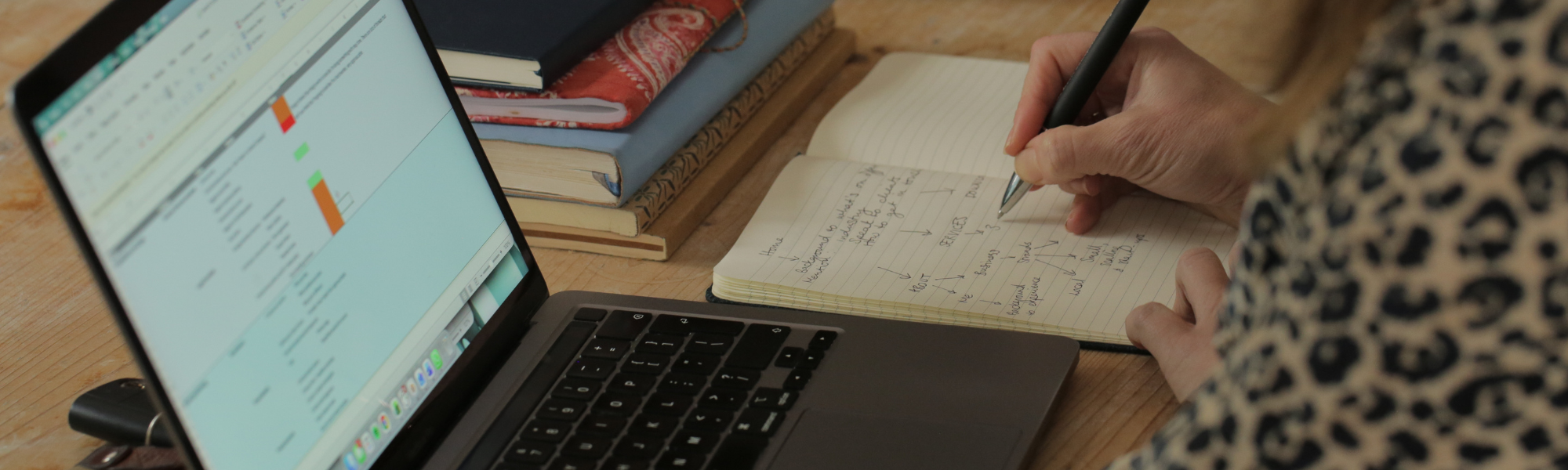 Marketing desk set up with laptop and notebook, woman writing a list