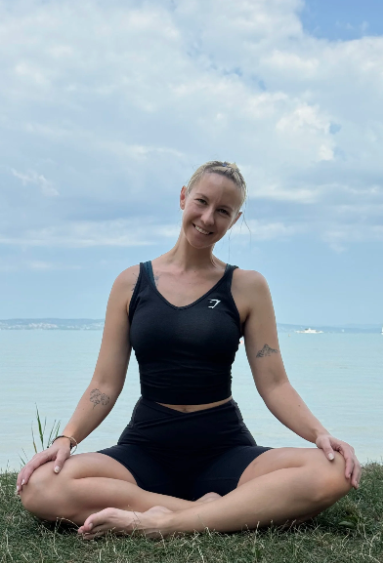 A woman practicing yoga outdoors near a body of water on a cloudy day.
